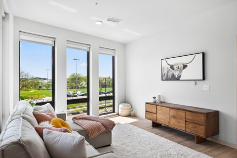 A living room with a couch, a painting of a cow, and a large window.
