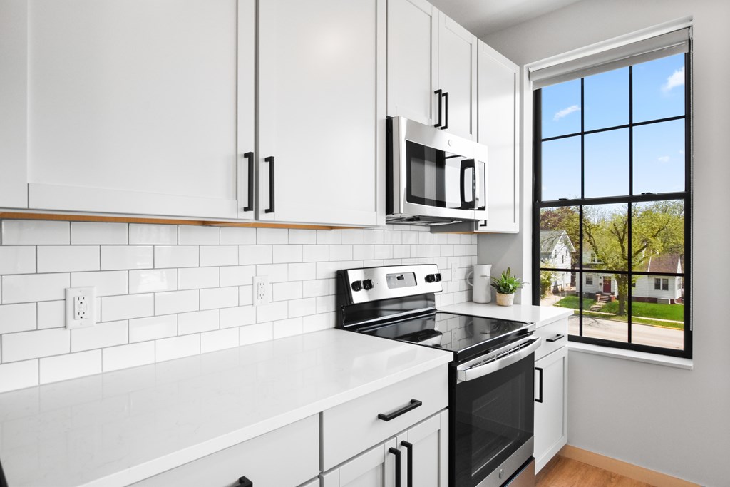 A kitchen with white appliances and cabinets with a window overlooking a green area.