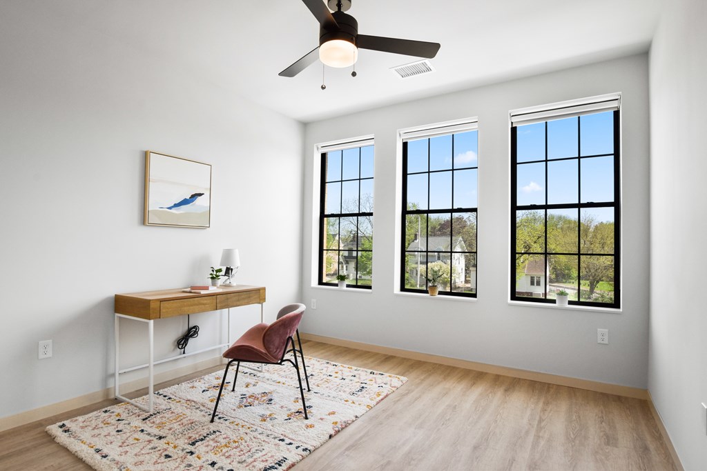 A room with a desk, chair, and a ceiling fan.