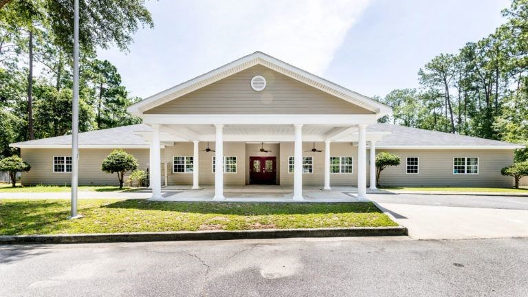 A church with a white facade and a red door is surrounded by greenery.