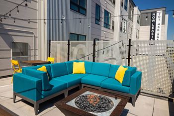 a seating area with a blue couch and yellow pillows in front of a building at The Landing at 1001 NP, Fargo, North Dakota 58102