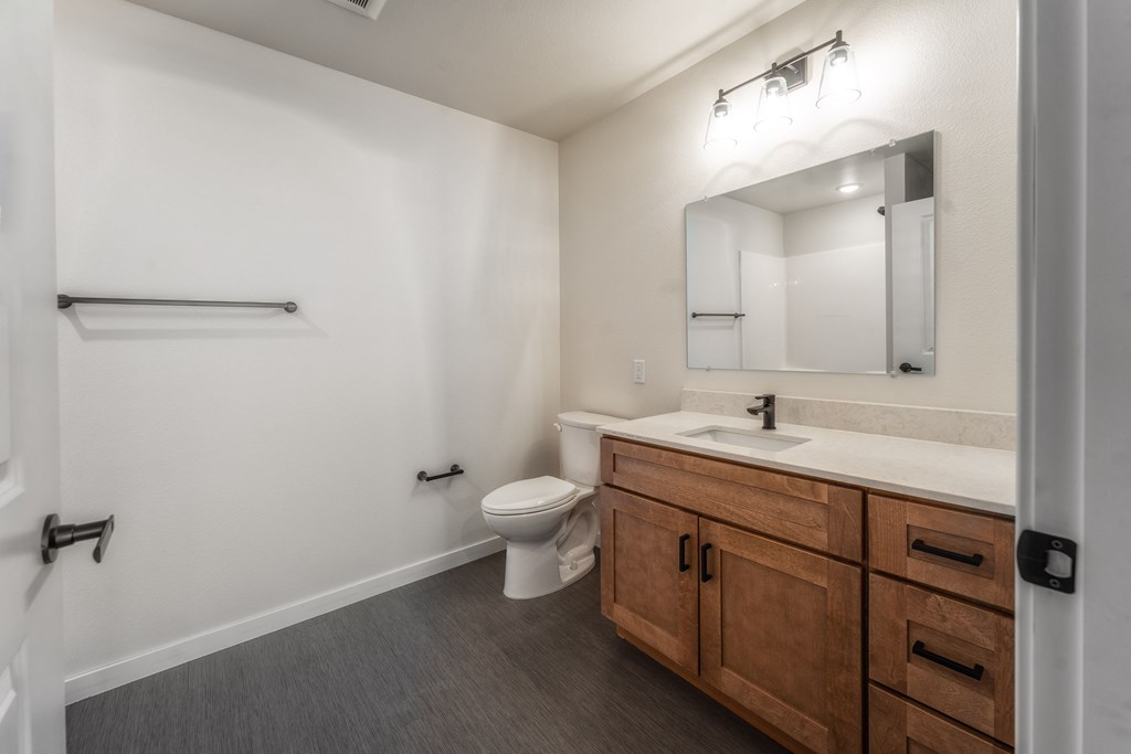 A bathroom with a toilet, sink, and mirror. at Unite Apartments, North Dakota