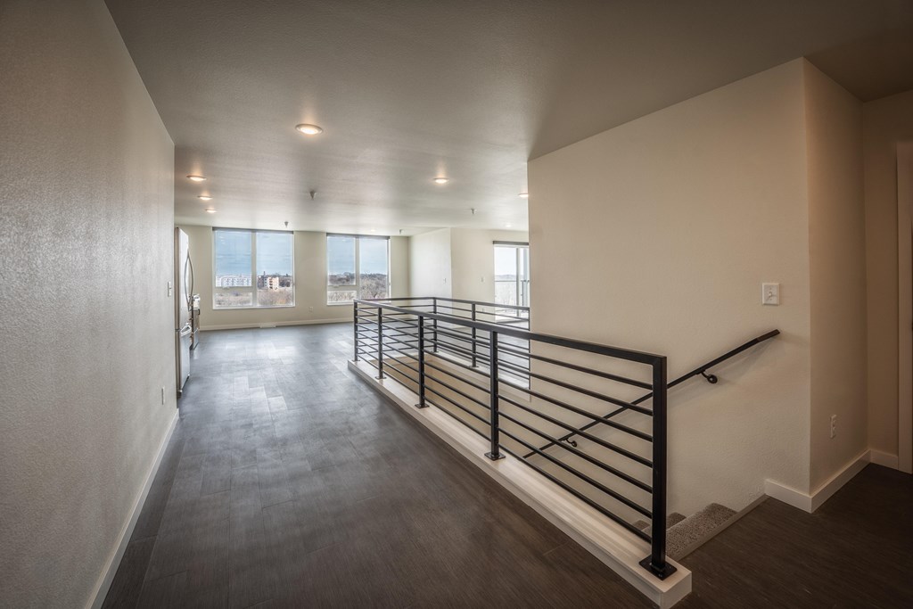 A long hallway with a black railing and a window with a view. at Unite Apartments, North Dakota, 58103