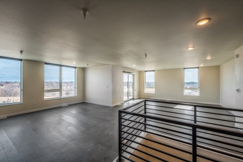 A large empty room with a balcony and a view of trees outside.