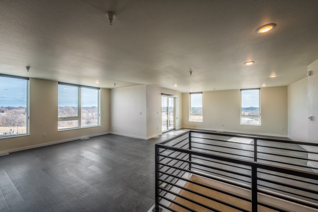 A large empty room with a balcony and a view of trees outside.