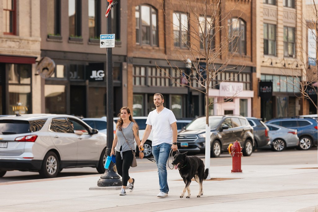 A man and a woman walking a dog down a city street  at Mercantile on Broadway, Fargo, ND 58102