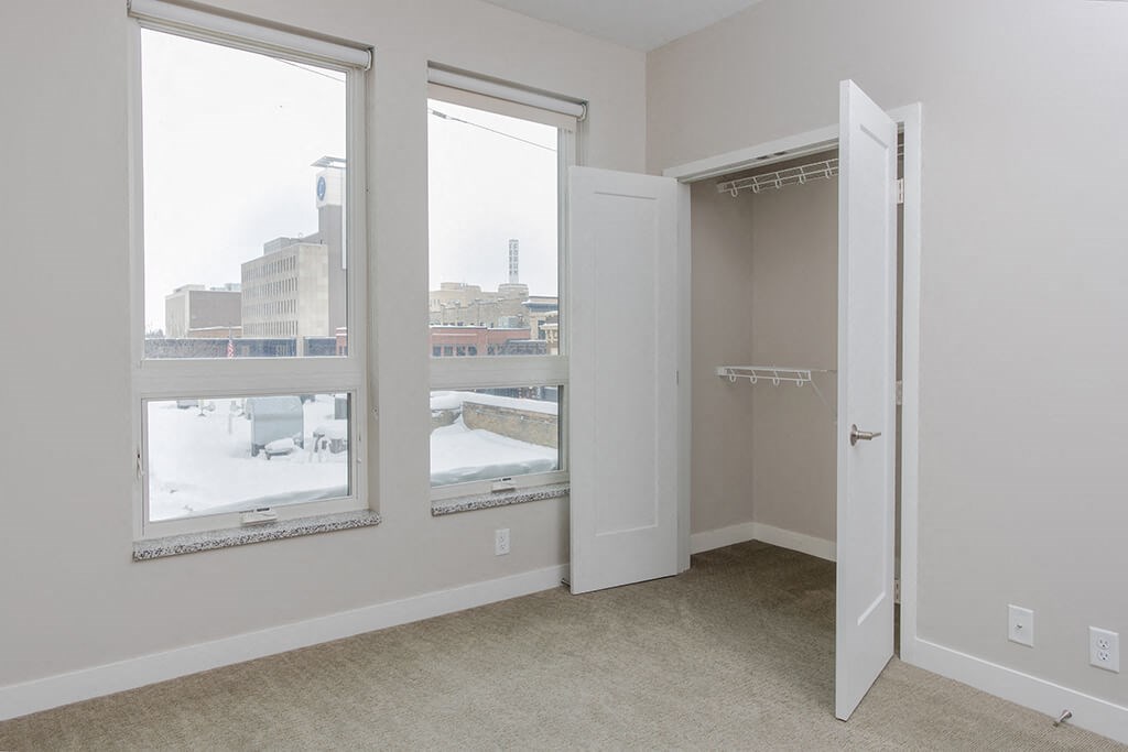 a bedroom with three large windows and a closet  at RoCo Apartments, Fargo, North Dakota 58102