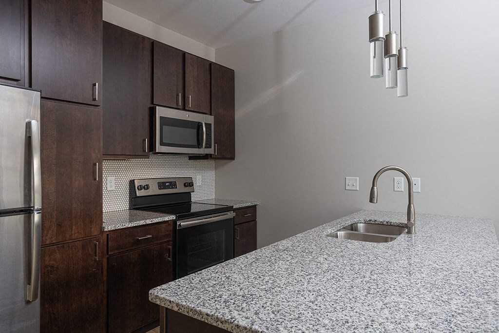 a kitchen with granite countertops and dark wood cabinets  at RoCo Apartments, Fargo, North Dakota 58102