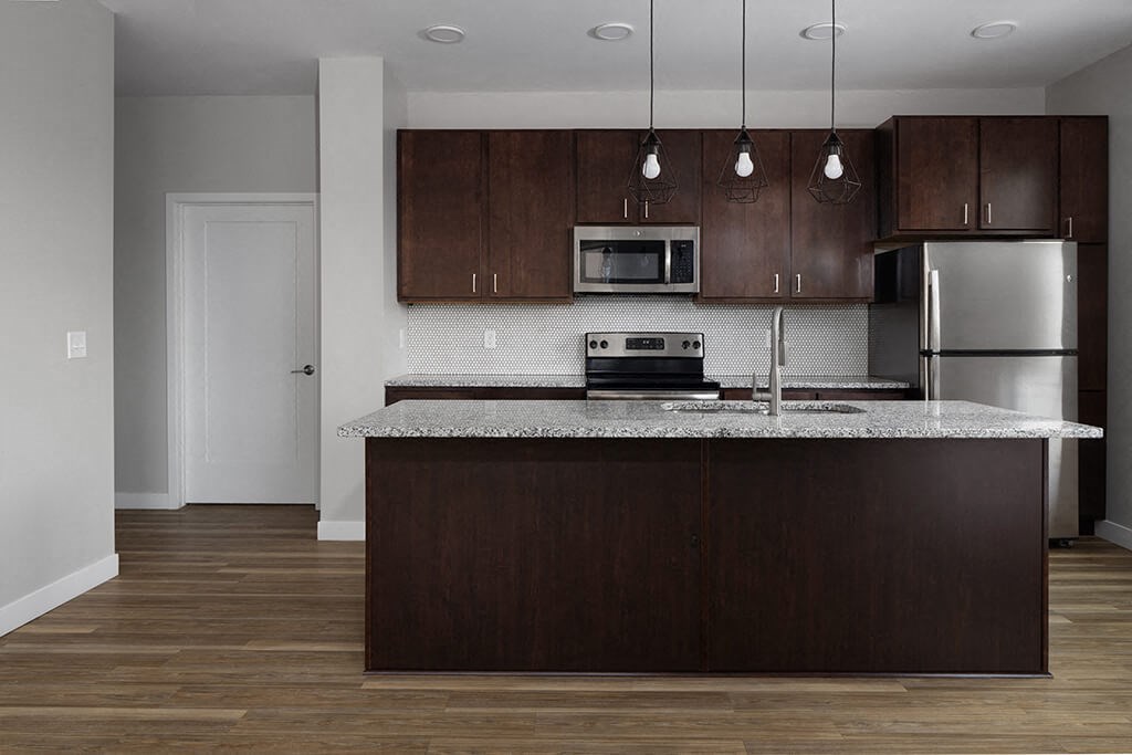 a kitchen with a large island with granite countertops and dark wood cabinets  at RoCo Apartments, Fargo, North Dakota, 58102
