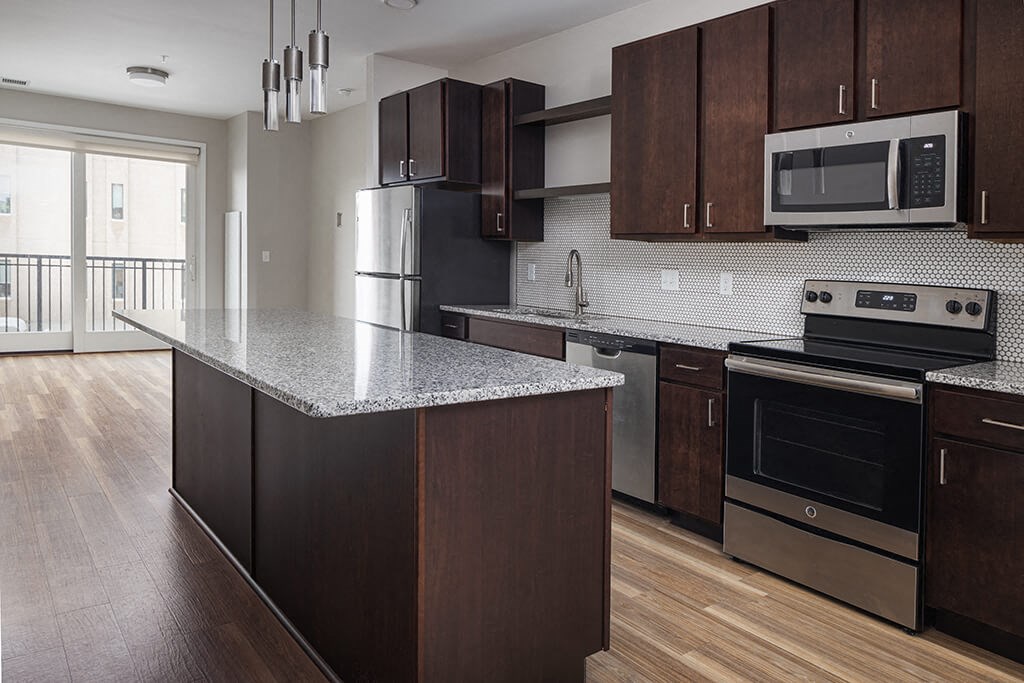 a kitchen with dark wood cabinets and an island with a granite countertop and stainless steel appliances  at RoCo Apartments, Fargo, ND 58102