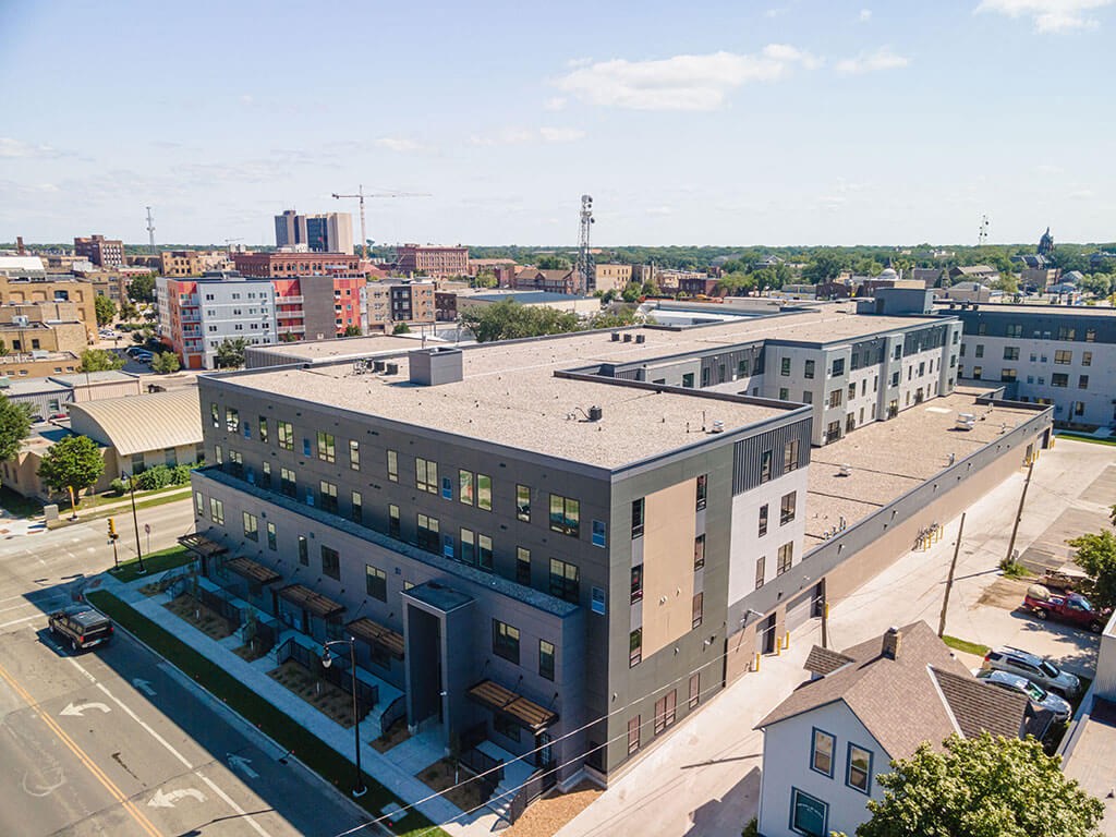 a large gray building with a gray roof and a city in the background at The Landing at 1001 NP, Fargo, North Dakota 58102