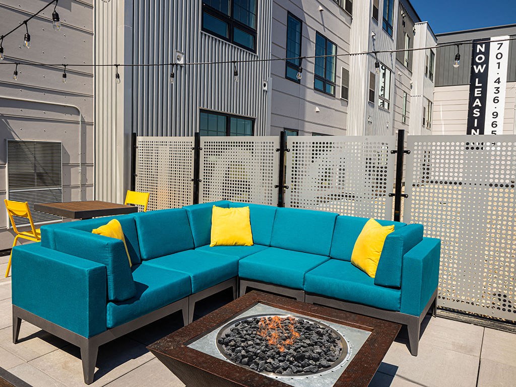 a patio with a blue couch and yellow pillows at The Landing at 1001 NP, Fargo, ND 58102