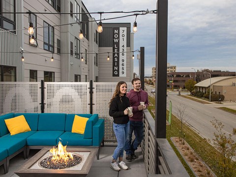 a man and a woman standing on a patio with a fire pit and a blue couch at The Landing at 1001 NP, Fargo, ND, 58102