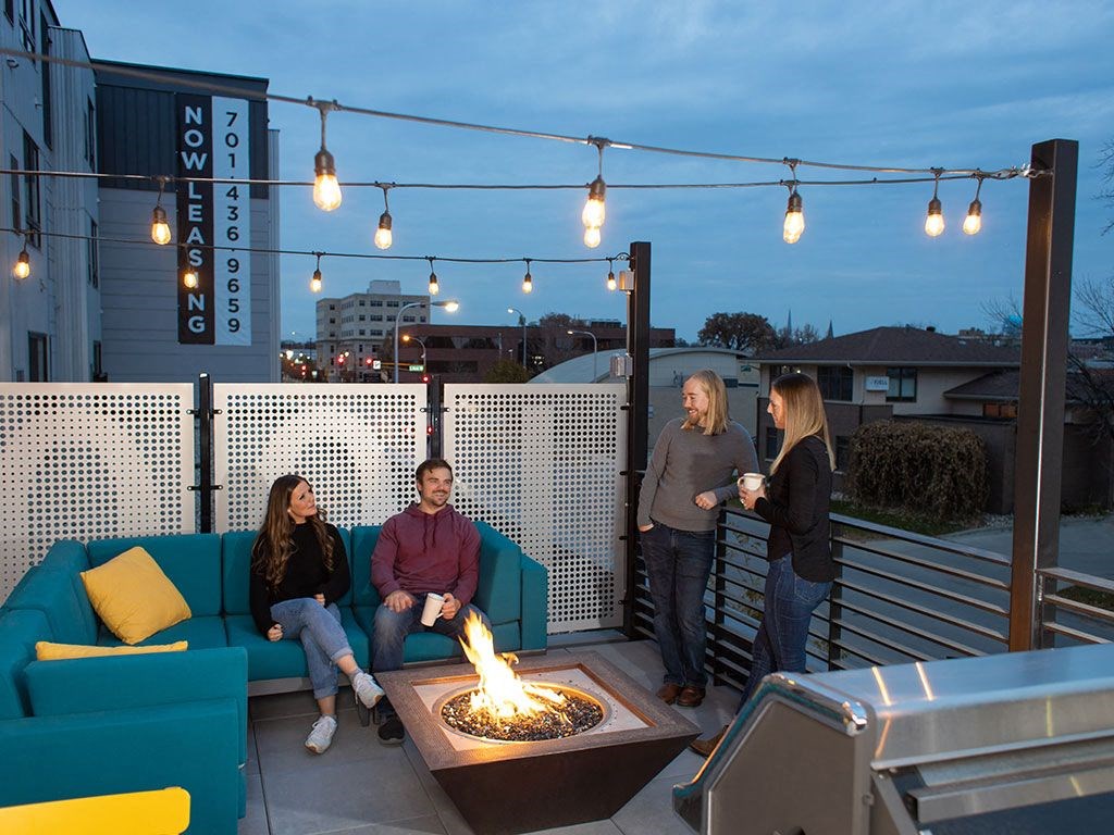 a group of people sitting around a fire pit on a rooftop patio at The Landing at 1001 NP, Fargo, ND 58102
