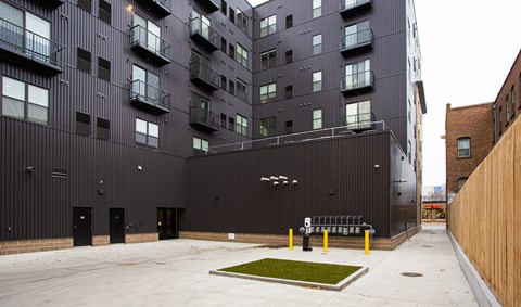 A courtyard with a bench and grass patch in front of a black building  at Mercantile on Broadway, Fargo, North Dakota 58102