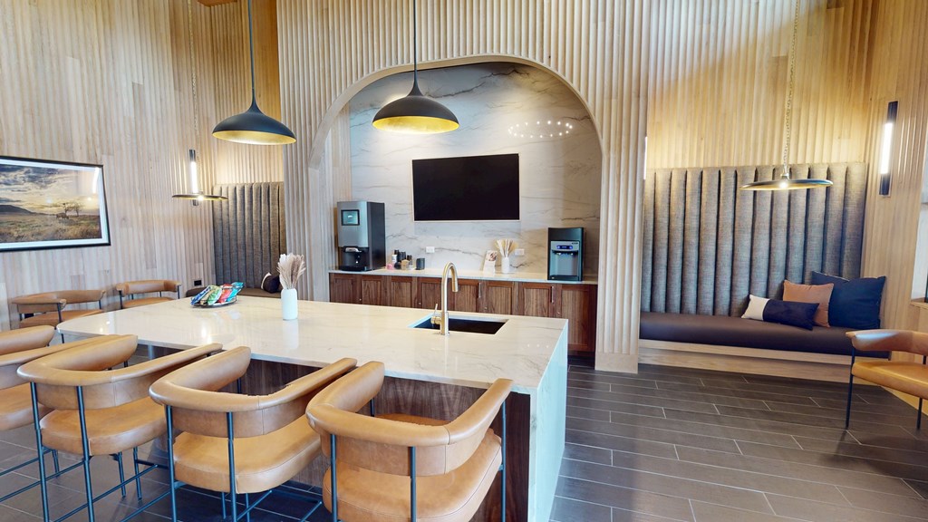 Modern kitchen here at Trailwinds Apartment Homes with wood paneling, marble island, and tan leather stools. Pendant lights hang above, with cozy seating and a wall-mounted TV. Warm ambiance.