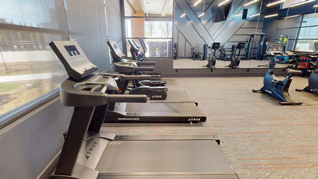 A treadmill with a digital display is in a gym with other exercise equipment.
