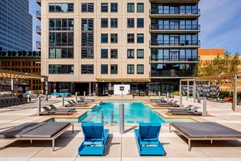 a swimming pool with chaise lounge chairs in front of a tall building