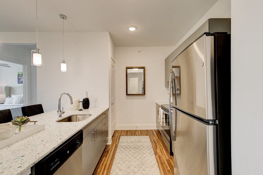 Modern kitchen here at  Florence at the Harbor Apartment Homes with glossy countertops, stainless steel fridge, and pendant lights. Wooden floor, neutral colors, and a cozy, inviting atmosphere.