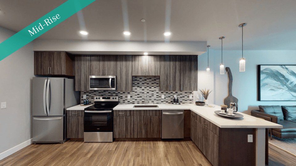 Modern kitchen here at Capitol Towers Luxury Midrise Apartments with wood cabinets, stainless steel appliances, and mosaic backsplash. A cozy living area is visible, accented by pendant lights and artwork.