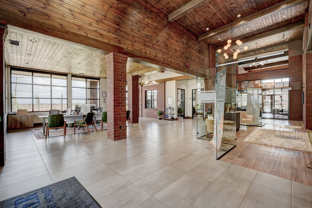 Spacious modern lobby here at 35 Degrees North Apartment Homes with brick pillars, large windows, and warm wood ceiling. Green chairs around desks create a welcoming, airy atmosphere.