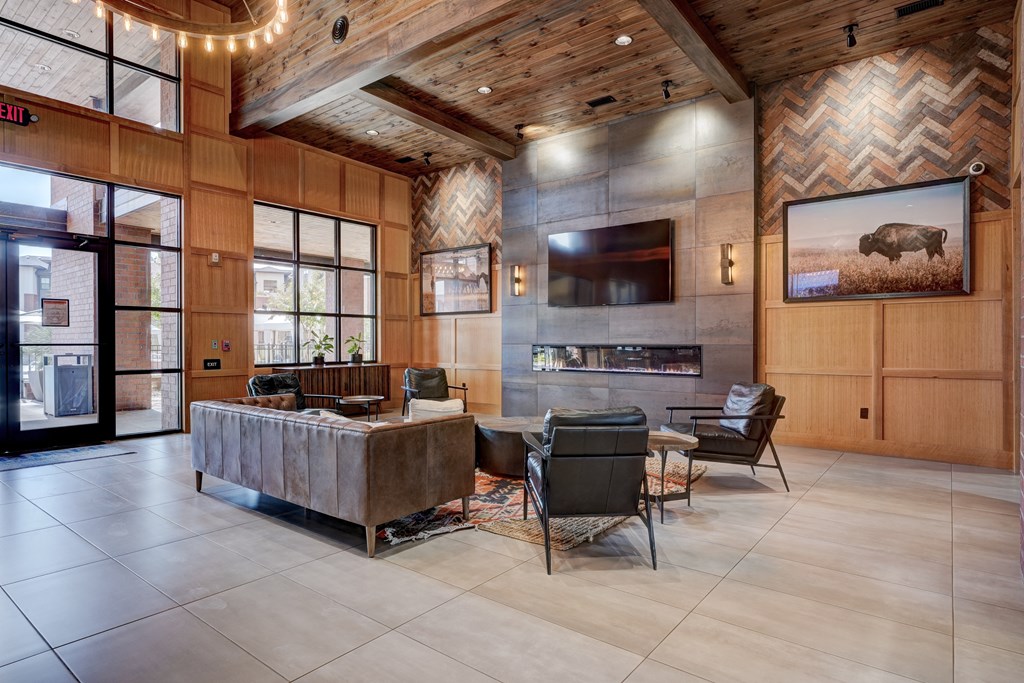 Spacious lobby here at 35 Degrees North Apartment Homes with cozy seating, leather couches, and armchairs. Modern decor includes a wall-mounted TV, fireplace, and buffalo artwork. Warm, inviting ambiance.