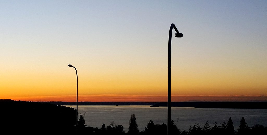 a sunset over a body of water and two street lights