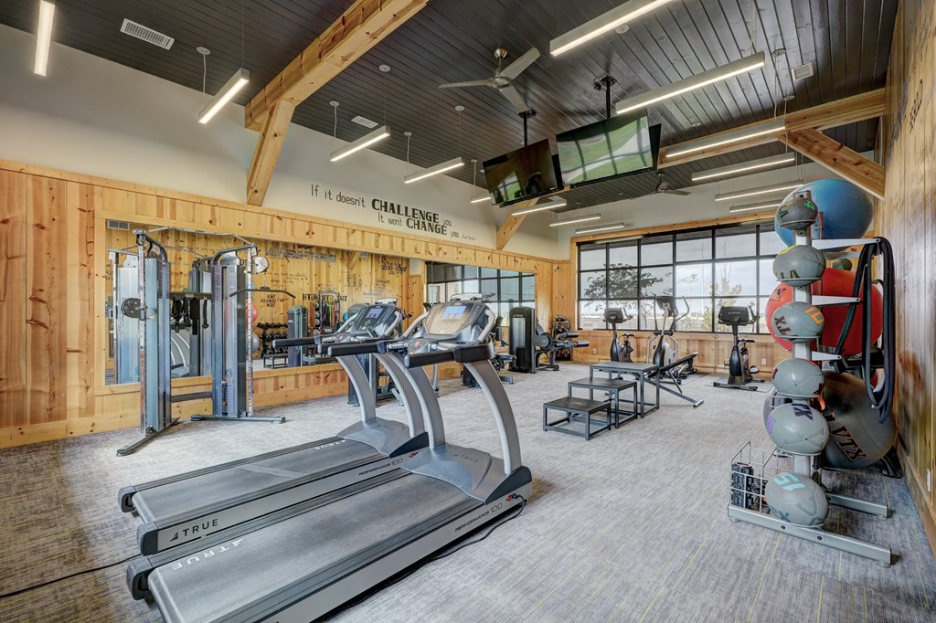 Spacious gym here at 35 Degrees North Apartment Homes with wooden walls, treadmills, weight racks, exercise balls, and rowing machines. Bright lighting and large windows create an energetic atmosphere.
