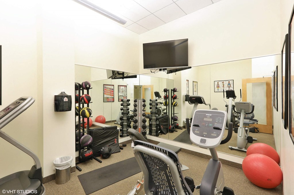 A gym with a variety of equipment including a treadmill, weights, and a television.