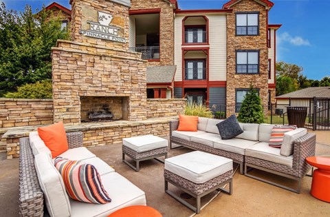 A patio area with a couch, pillows, and a fireplace in front of a building.