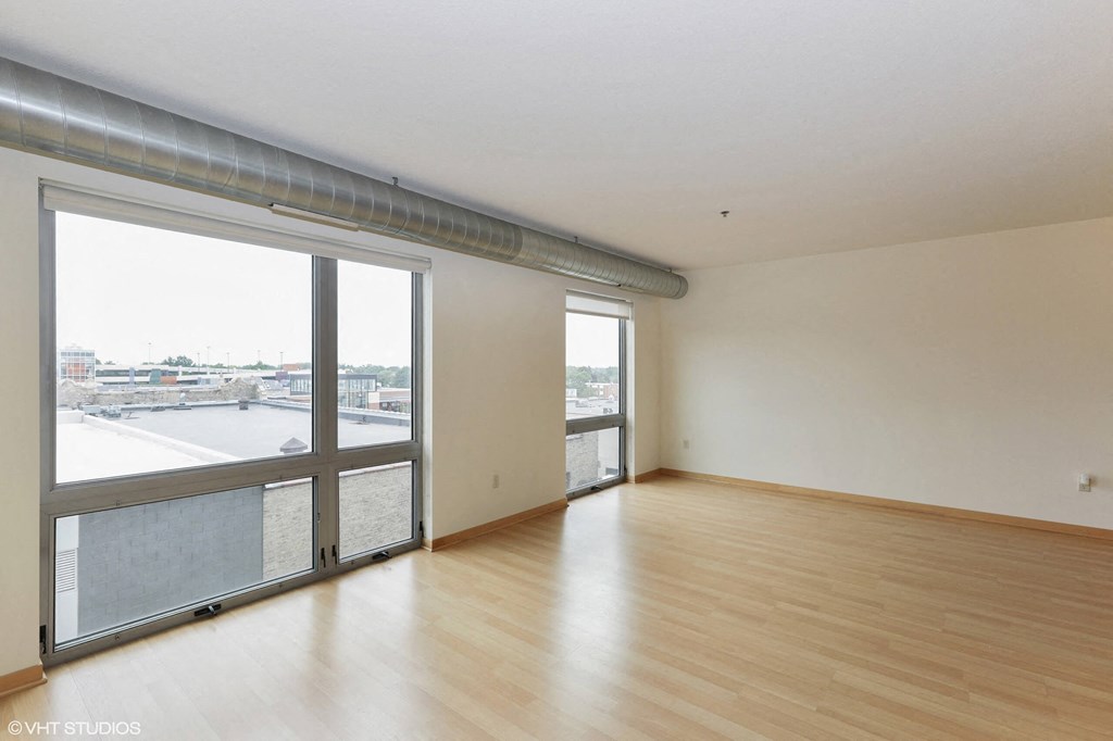 A room with wooden floors and a large window with a view of a parking lot.