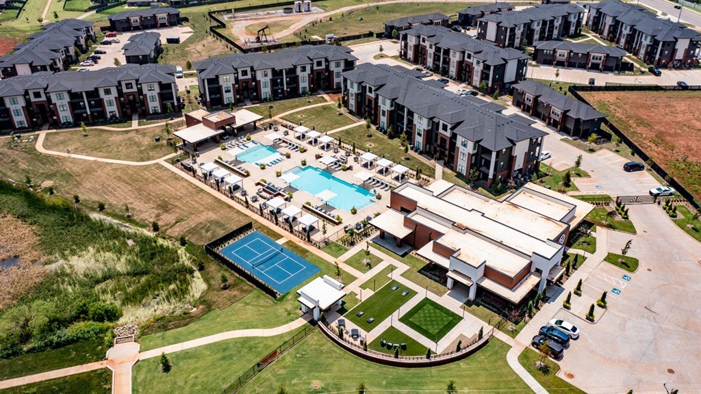 Aerial view of 35 Degrees North Apartment Homes complex with modern buildings, a large central pool surrounded by loungers, and a tennis court, set in a landscaped area.