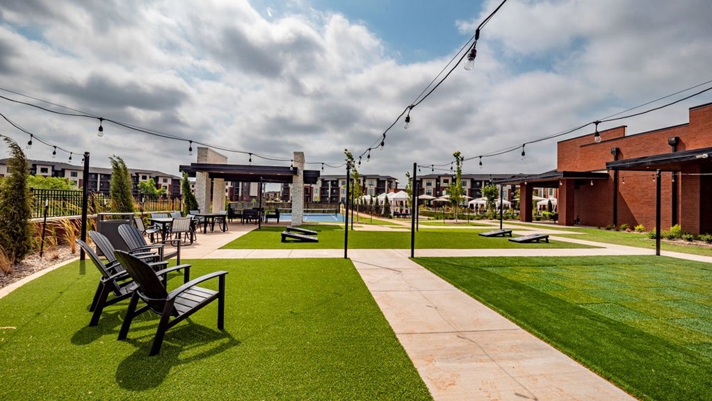 Outdoor patio here at 35 Degrees North Apartment Homes with artificial grass, Adirondack chairs, string lights, and a modern fire pit. Overcast sky adds a calm, inviting atmosphere.