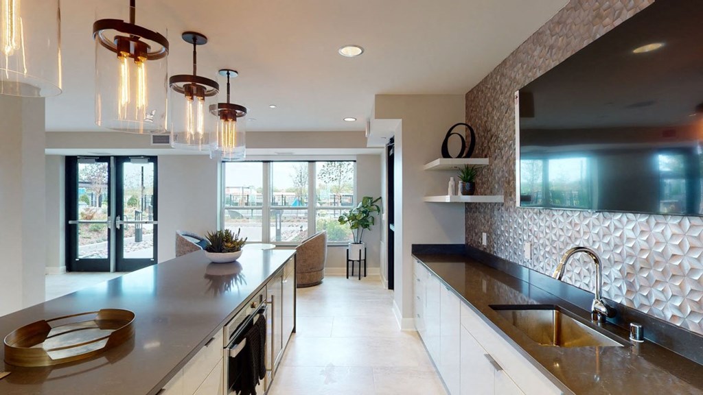 Modern kitchen here at The Collection at Highland Bridge Apartment Homes with a sleek island, pendant lights, and textured backsplash. Large windows brighten the space, giving it an open, airy feel.