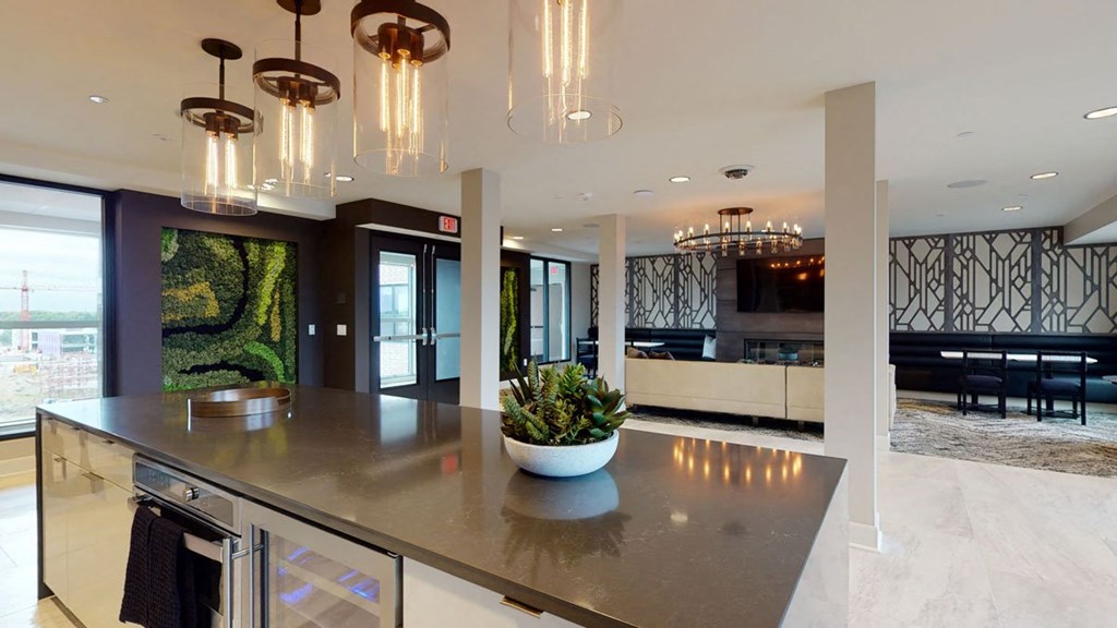 Modern lounge here at The Collection at Highland Bridge Apartment Homes with a sleek island counter topped with a plant centerpiece. Elegant lighting and geometric wall decor create a cozy, upscale ambiance.