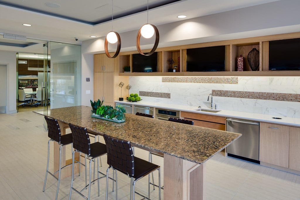 Modern kitchen here at Inspire Apartment Homes with a granite island, high chairs, pendant lights, and succulents. Wooden cabinets and marble backsplash create a sleek, inviting atmosphere.