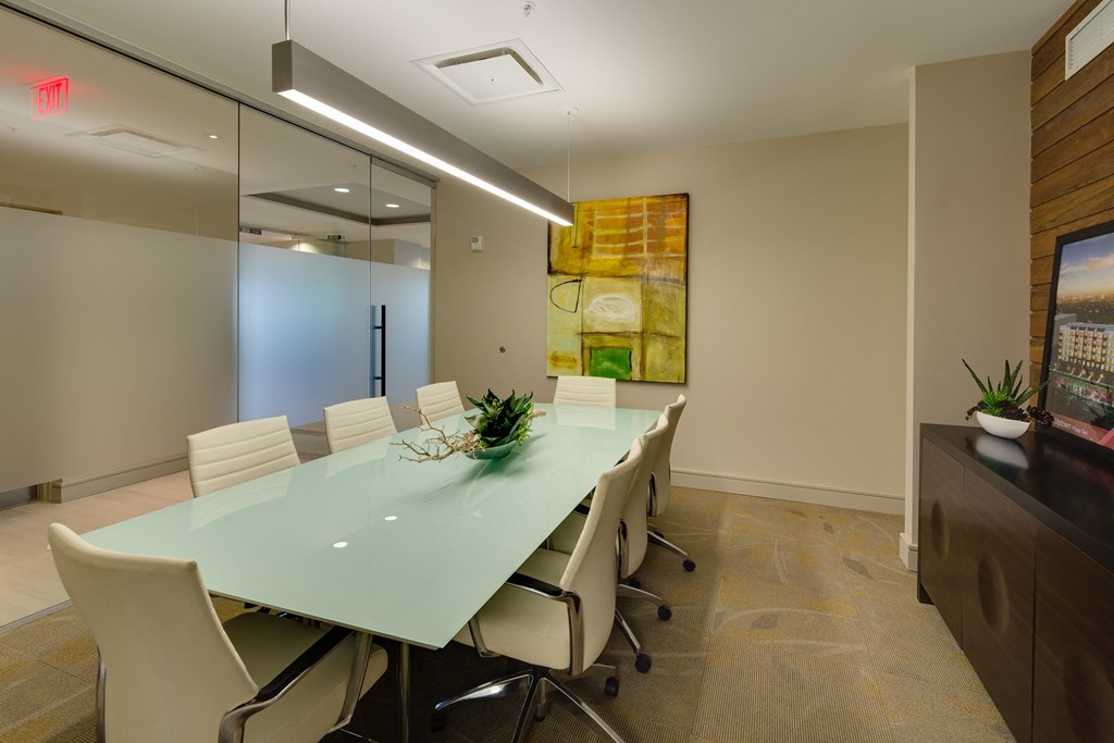 Modern conference room here at Inspire Apartment Homes with a frosted glass table, eight white chairs, abstract wall art, plants, and soft lighting, conveying a calm, professional tone.