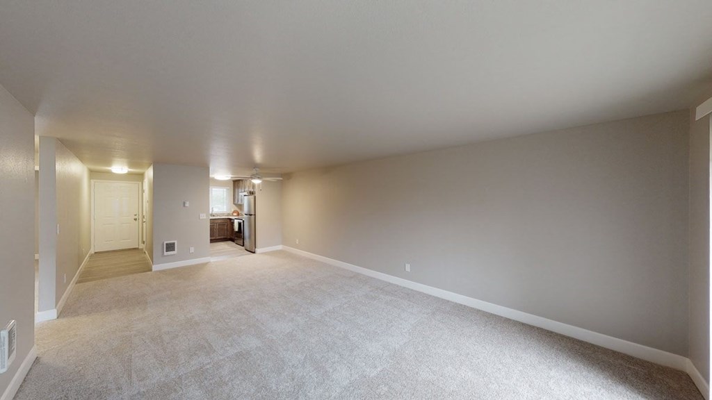 an empty living room with a kitchen in the background