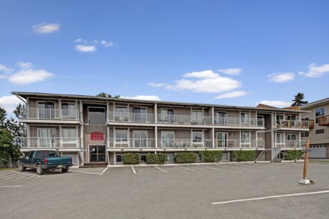 Arbor Pointe three-story apartment building with private balconies, exterior stair entry, and front parking lot under a bright blue sky.