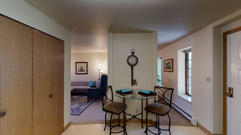 A dining room with a table set for two and a couch in the background.