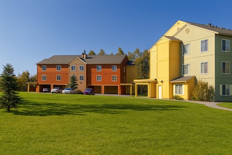 A large building with a yellow section is surrounded by a green lawn.