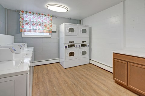 A laundry room with a washer and dryer, a window with a floral curtain, and a wooden cabinet.
