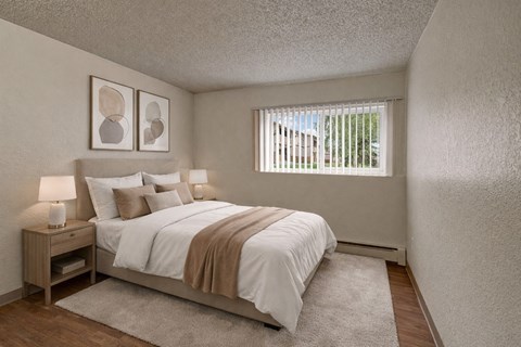 A warm and inviting bedroom here at The Greenbriar featuring a neatly made bed with crisp white bedding, layered neutral accent pillows, a soft beige throw blanket, matching nightstands with modern lamps, abstract wall art above the headboard, wood-style flooring, a plush area rug, and a window with vertical blinds providing natural light and a peaceful outdoor view.
