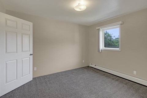 A room with a white door and a window with a view of trees outside.