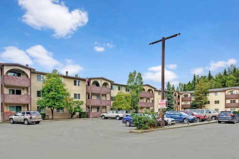 A parking lot in front of apartment buildings with cars parked.