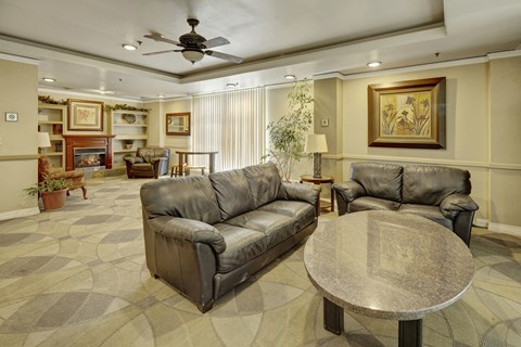 A spacious community lounge here at Mendenhall-Tower with leather sofas, a round granite table, and a warm fireplace framed by built-in shelving.