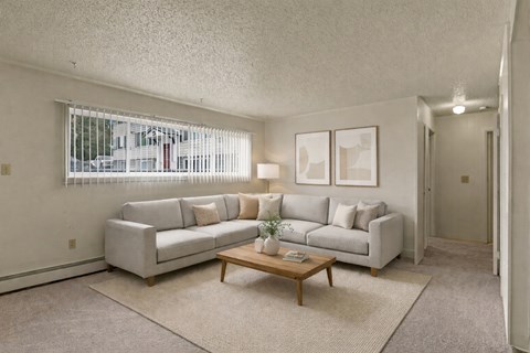 A living room with a grey couch, a coffee table, and a window with blinds.