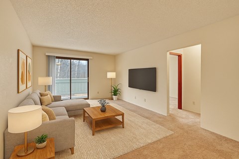 A living room with a grey couch, a wooden coffee table, a flat screen TV, and a large window.