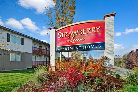 A sign for Strawberry Lane Apartment Homes is in front of a building.