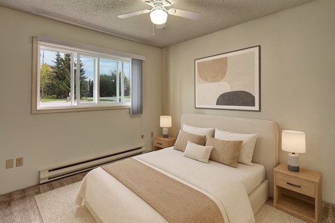 A bedroom with a large bed, a ceiling fan, and a window with a view of trees.